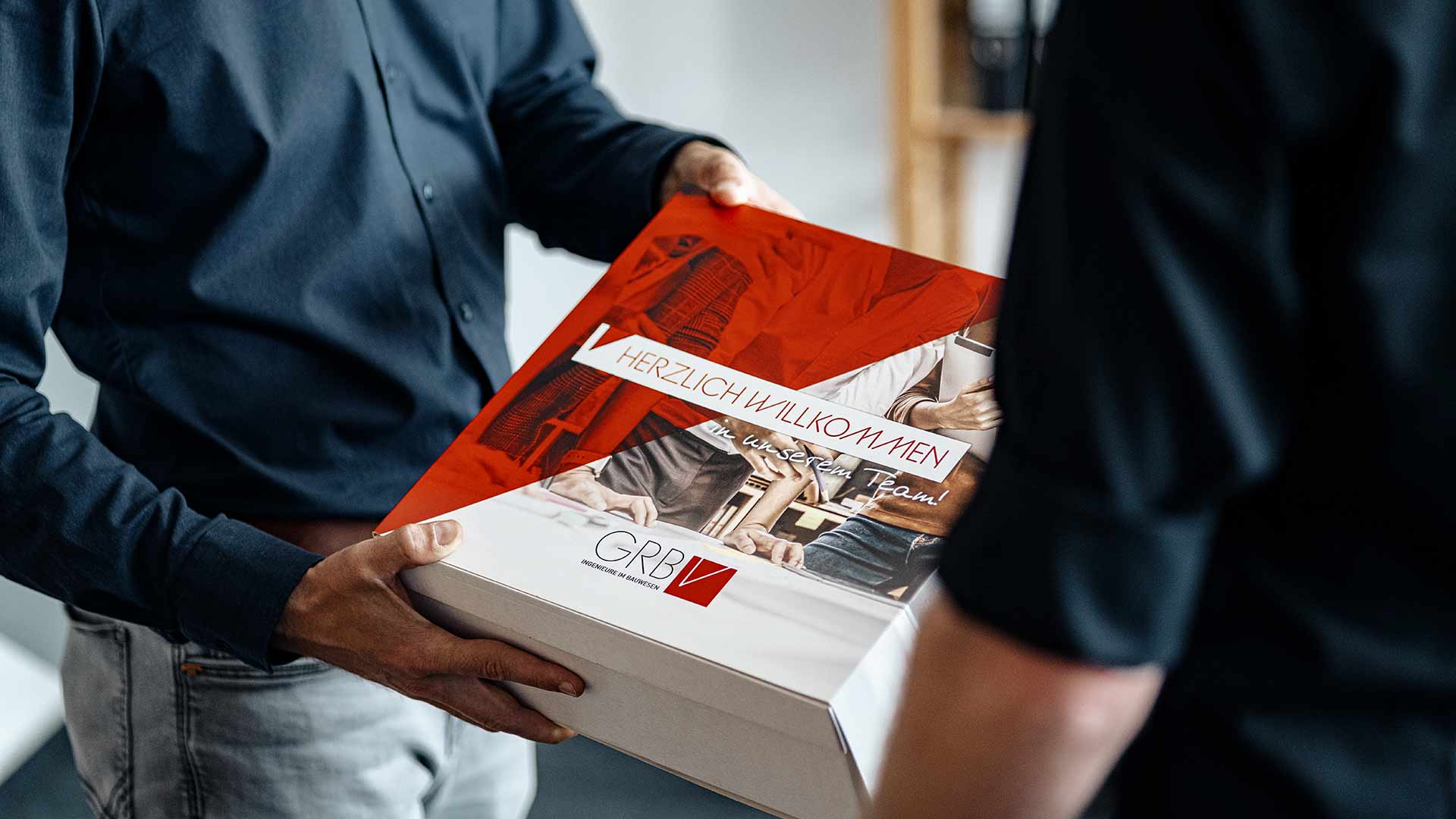 GRBV Herzlich Willkommens Box Das Bild zeit die Übergabe einer "Herzlich Willkommen" Box an einen neuen Mitarbeiter.