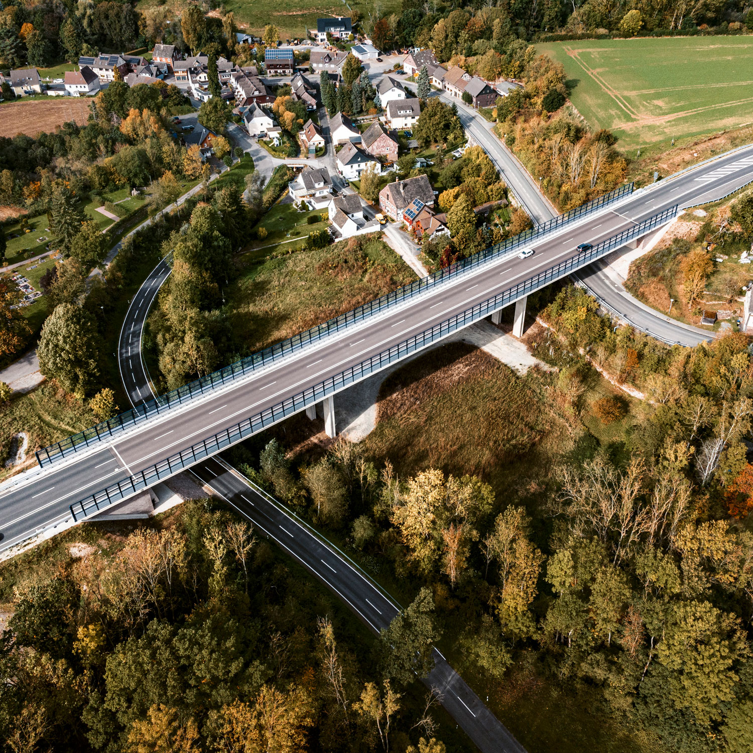 Referenz Talbrücke Negenborn Vogelperspektive auf eine Autobahn, die durch eine Landschaft mit einem Dorf und Feldern führt.